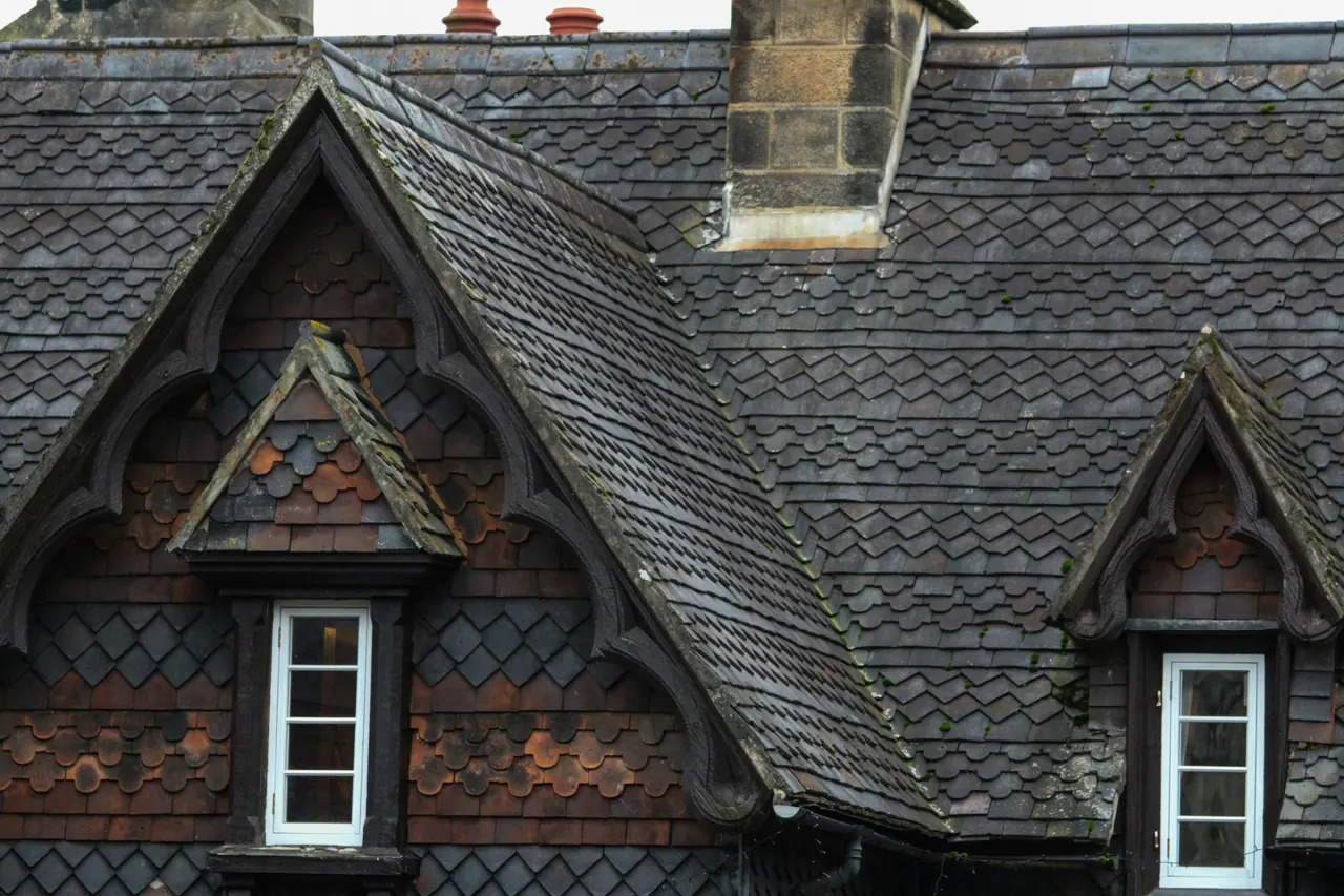 Slate roof with two pointed dormer windows and a stone chimney