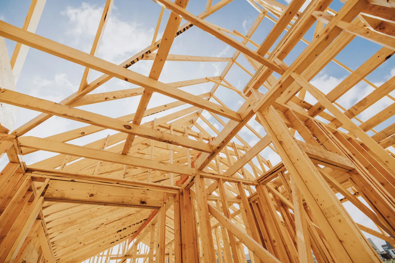 Looking up through new wood wall framing and roof trusses at a pale blue sky