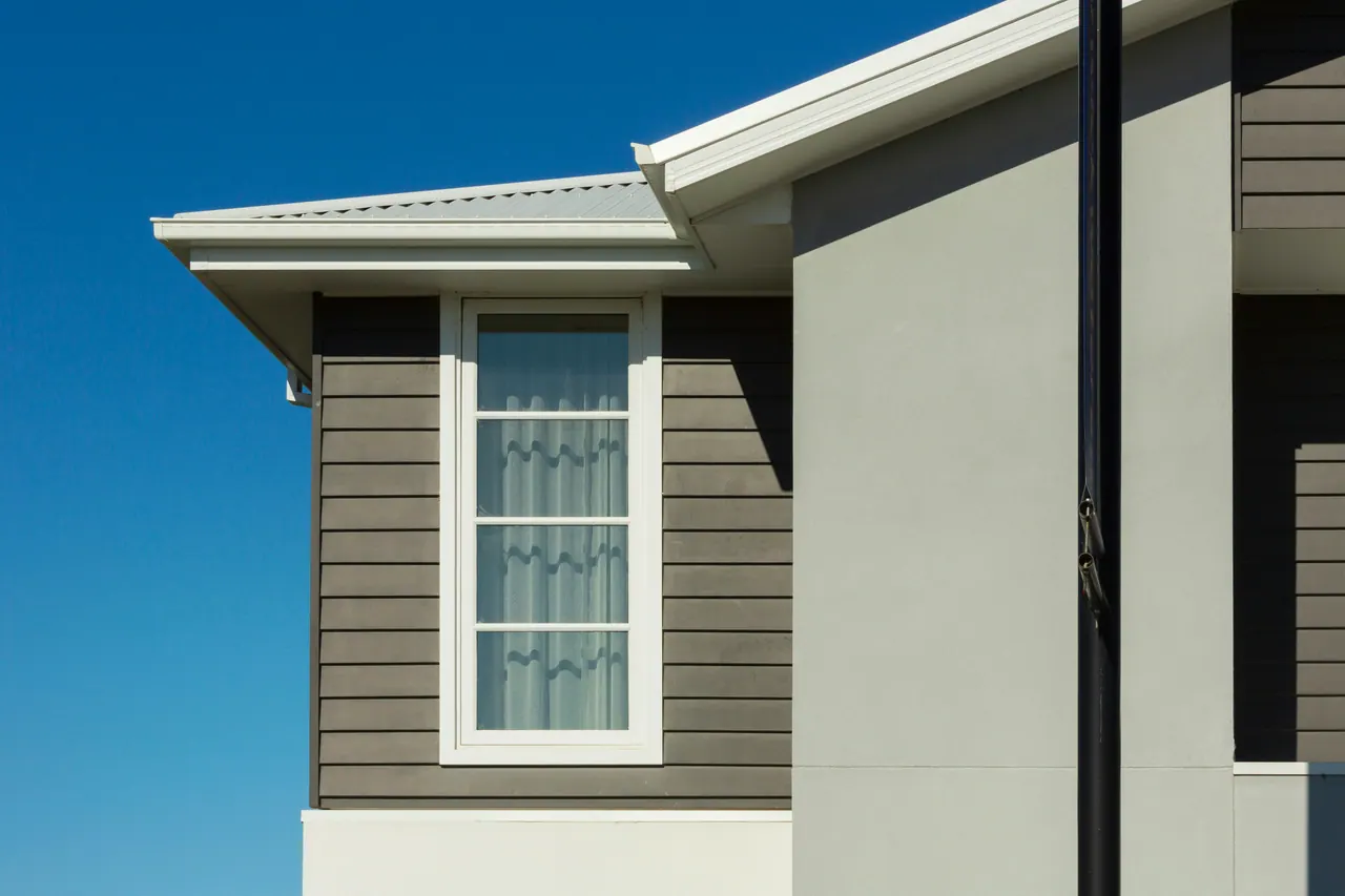 Corner of a new home with gray lap siding, a white-framed window and a clean roofline against blue sky