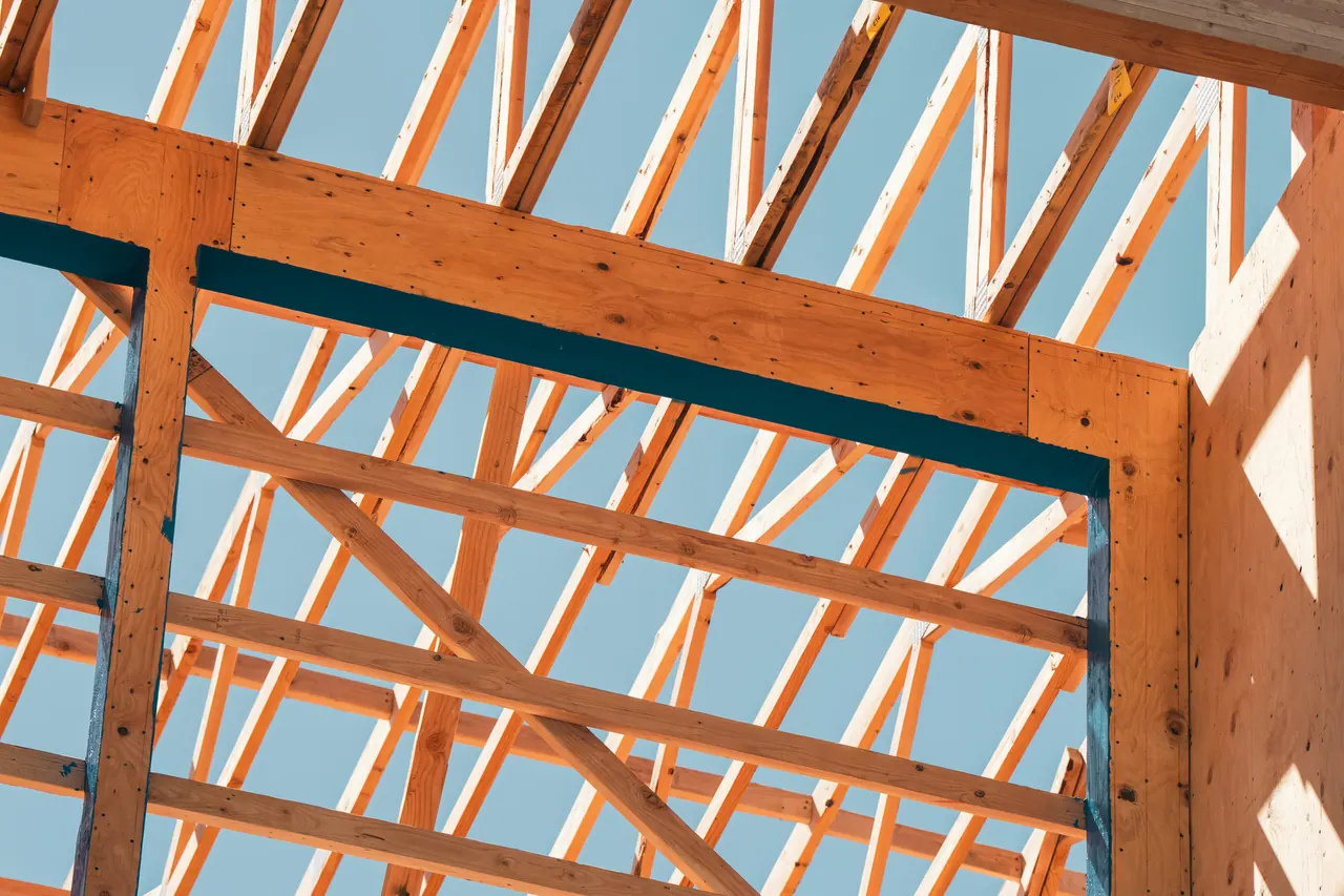 Wood roof trusses and a framed wall opening against a clear blue sky