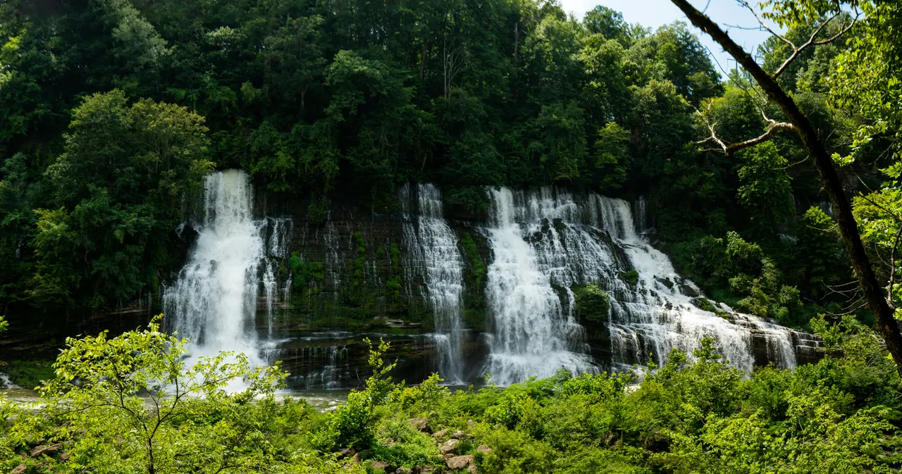 Several waterfalls spilling down a green, tree-covered bluff