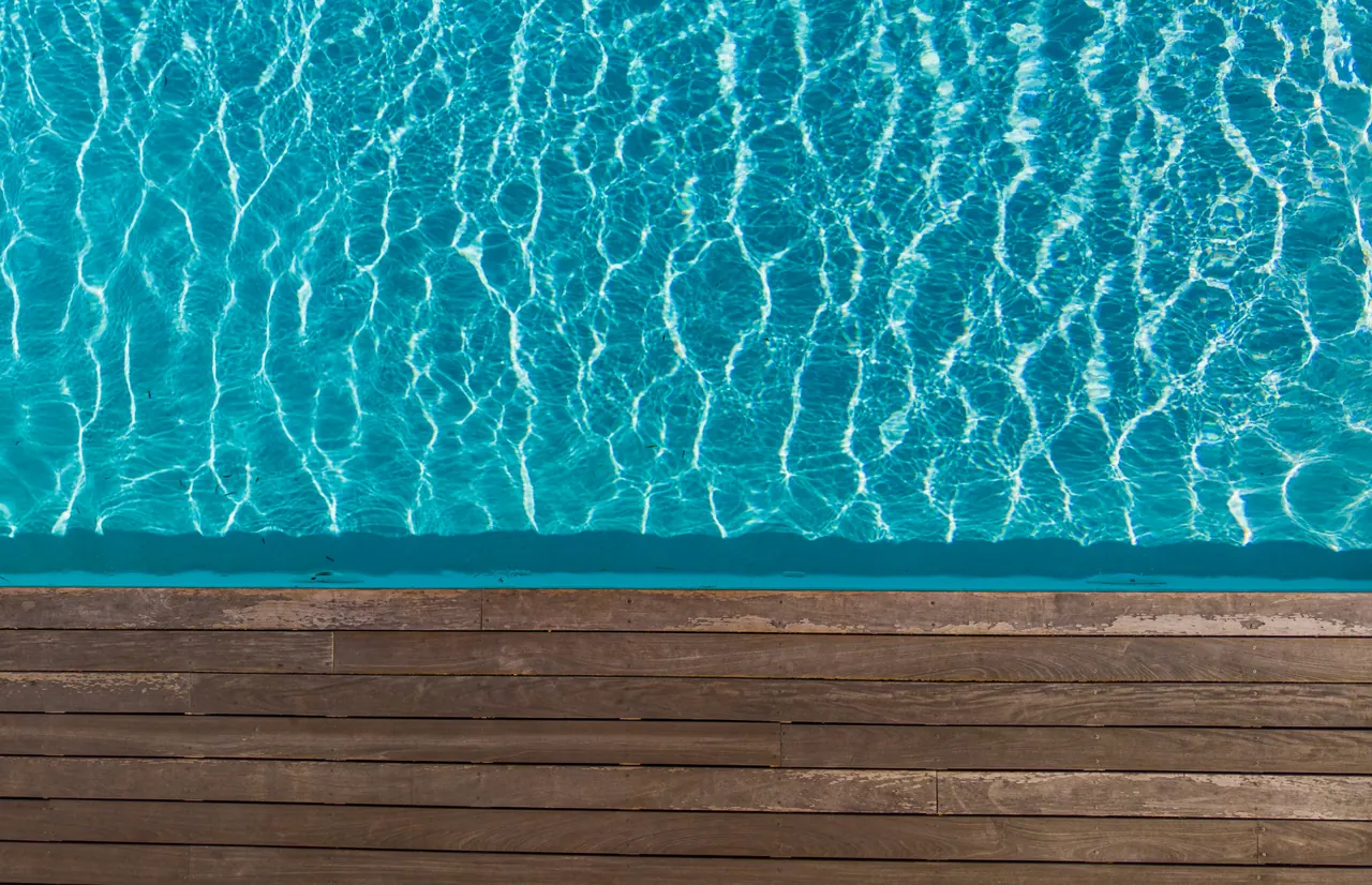 Overhead view of turquoise pool water beside a wooden deck